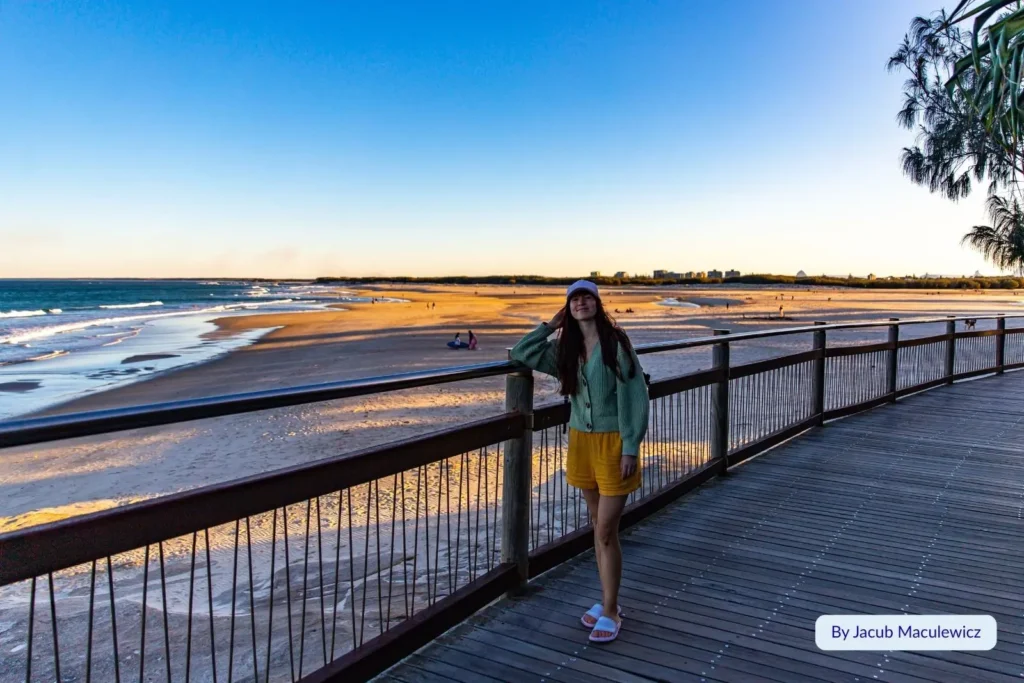 Boardwalk overlooking Kings Beach, Caloundra, Sunshine Coast, Queensland — woman enjoying the coastal views at sunset with calm water and golden sand below.