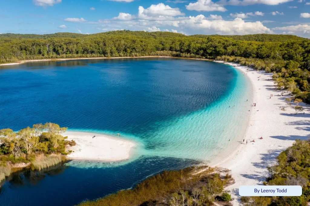 Aerial view of Lake McKenzie (Boorangoora) on Fraser Island (K’gari) showing brilliant turquoise water and pure white silica sand surrounded by lush rainforest.