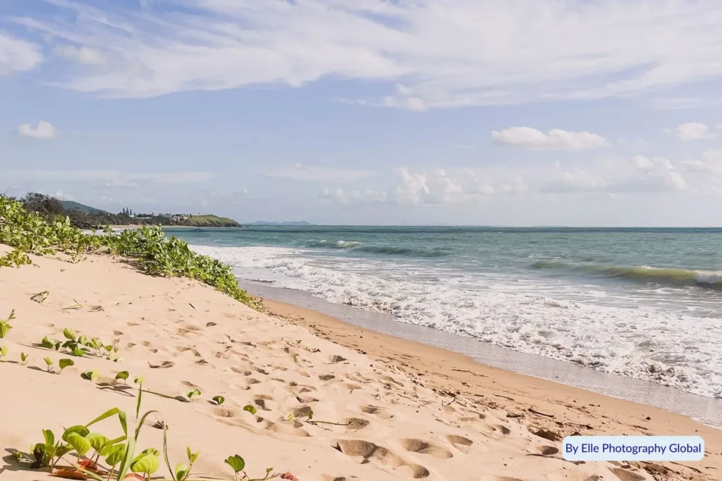 Golden sand and gentle waves along Lammermoor Beach on the Capricorn Coast, Queensland, with distant headlands and greenery lining the shore.
