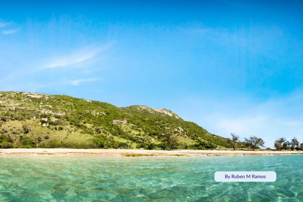 Turquoise waters and golden sand at Lizard Island, Queensland, surrounded by lush green hills and coral reef shallows.