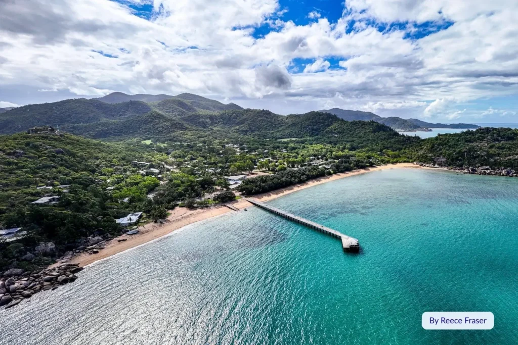 Scenic view of Magnetic Island jetty and coastal village with forested hills and clear blue ocean, Queensland, Australia.