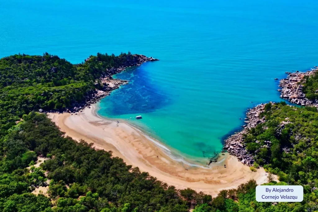 Aerial view of secluded bay with turquoise water and golden sand surrounded by granite headlands and bushland on Magnetic Island, Queensland.