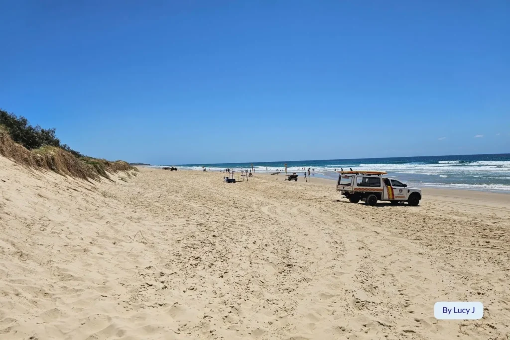 Patrolled section of Marcoola Beach, Sunshine Coast, Queensland, showing golden sand dunes, surf lifesaving vehicle, and open coastline.