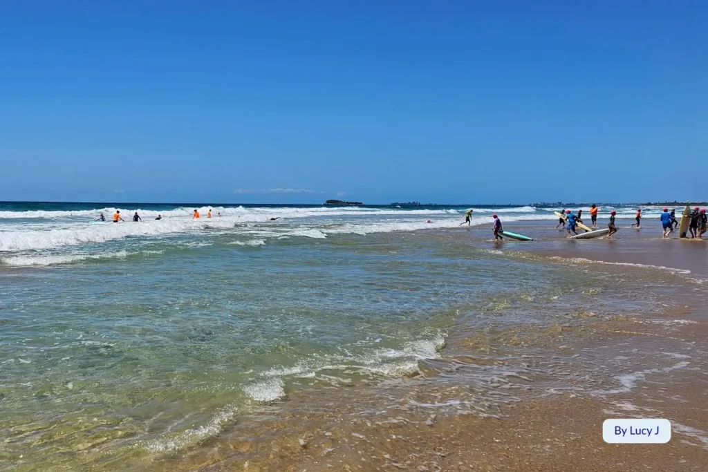 Swimmers and surfers enjoying the clear waves at Marcoola Beach, Sunshine Coast, Queensland, with gentle surf and golden sand under bright blue skies.