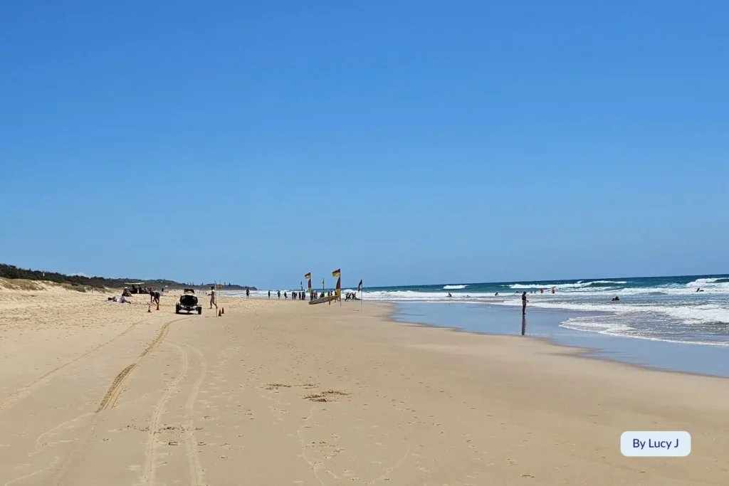 Wide sandy shoreline at Marcoola Beach, Sunshine Coast, Queensland, with lifeguard flags and beach patrol vehicles on a sunny day.