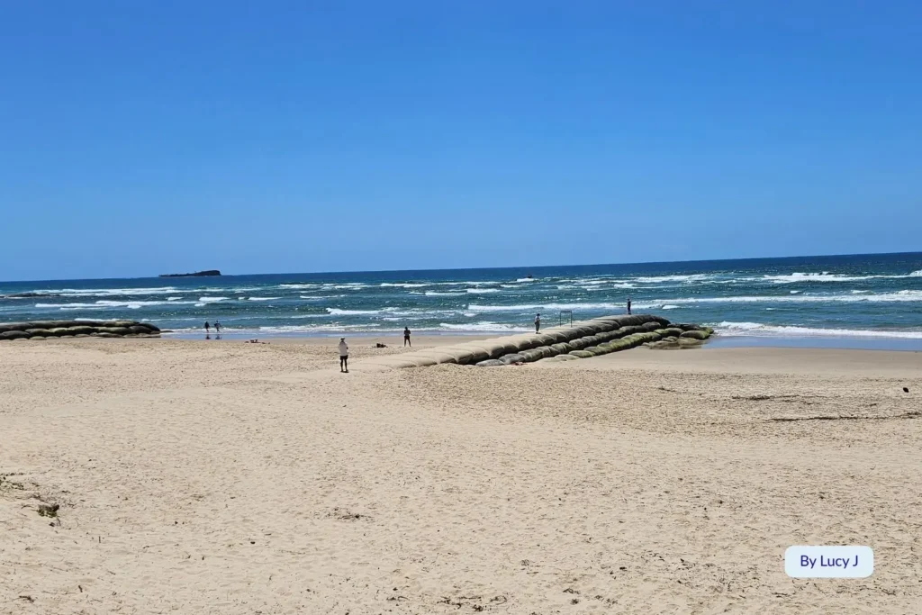Maroochydore Beach on the Sunshine Coast, Queensland, featuring sandbags near the shoreline, gentle waves, and views toward Mudjimba Island under clear blue skies.