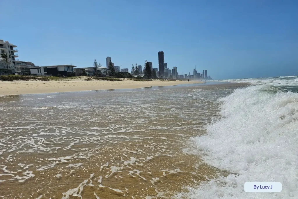 Foamy waves washing up on the golden shoreline of Mermaid Beach with the Surfers Paradise skyline in the distance, Gold Coast, Queensland, Australia.