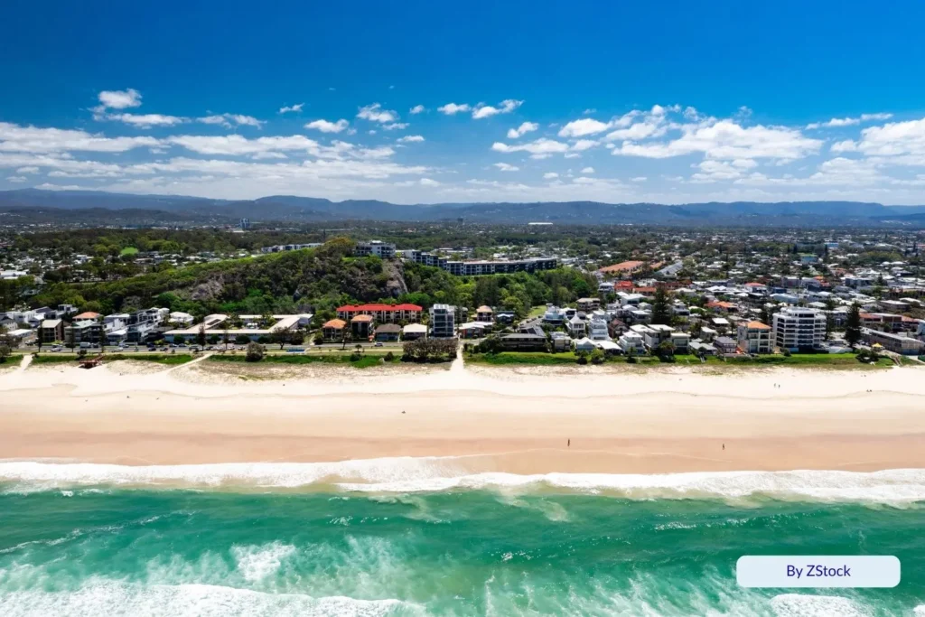 Aerial view of Miami Beach, Gold Coast, Queensland, showing turquoise waves, wide sandy shoreline, and coastal homes backed by green parkland and hills.
