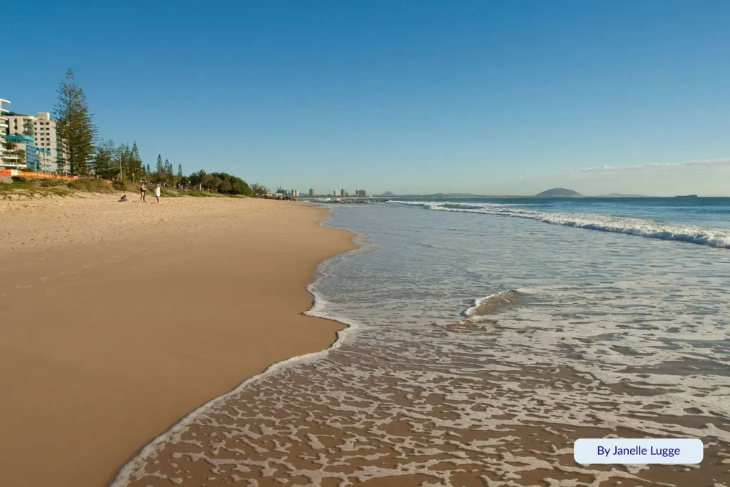 Wide sandy shoreline at Mooloolaba Beach, Caloundra region, Sunshine Coast — gentle waves meeting smooth sand with distant coastal skyline and Mount Coolum on the horizon.