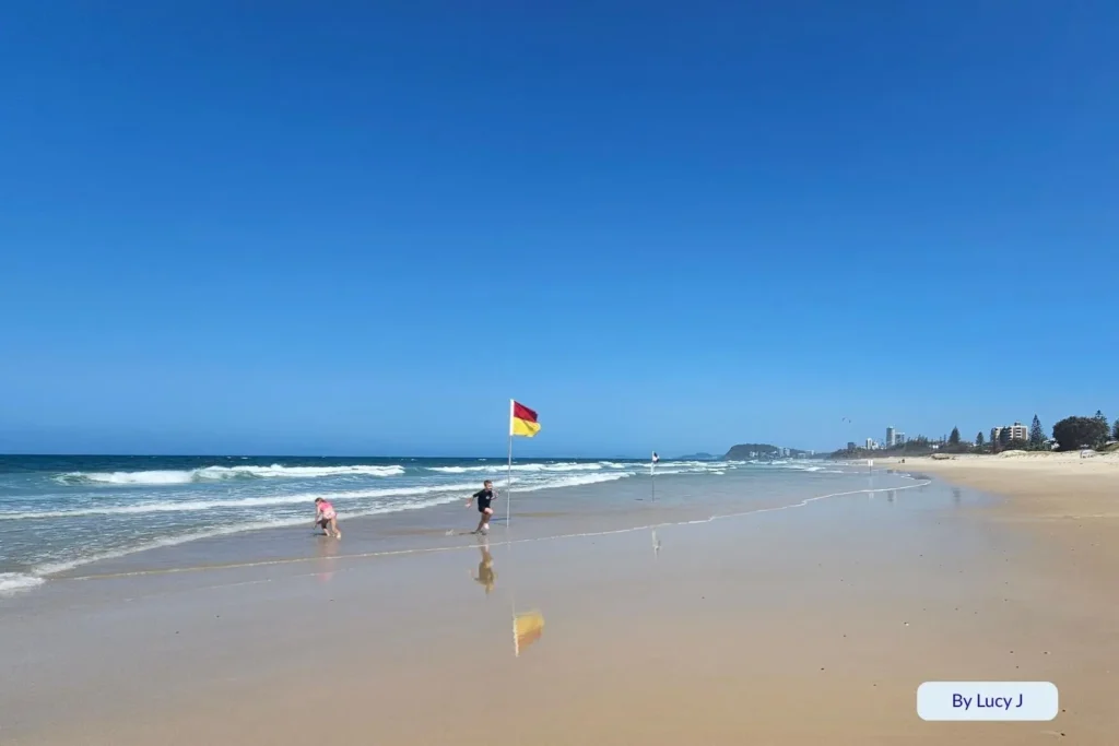 Children playing near the lifeguard-patrolled swimming area marked by red and yellow flags at Nobby Beach, Gold Coast, Queensland, Australia