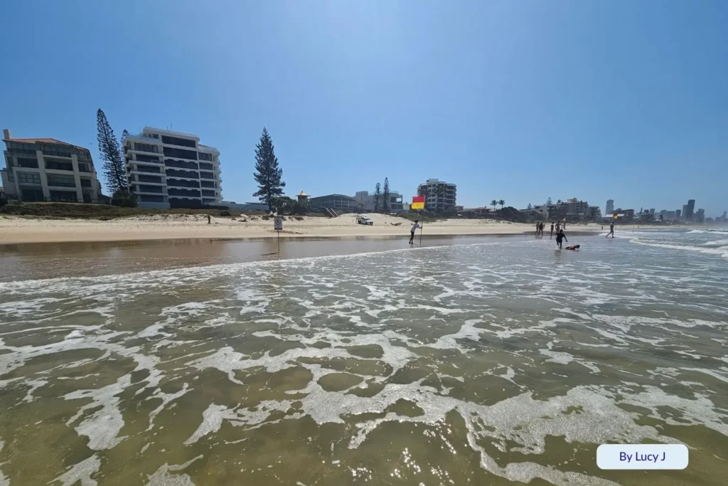 Foamy surf rolling onto the sand at Nobby Beach with beachfront apartments and the Gold Coast skyline in the distance, Queensland, Australia.
