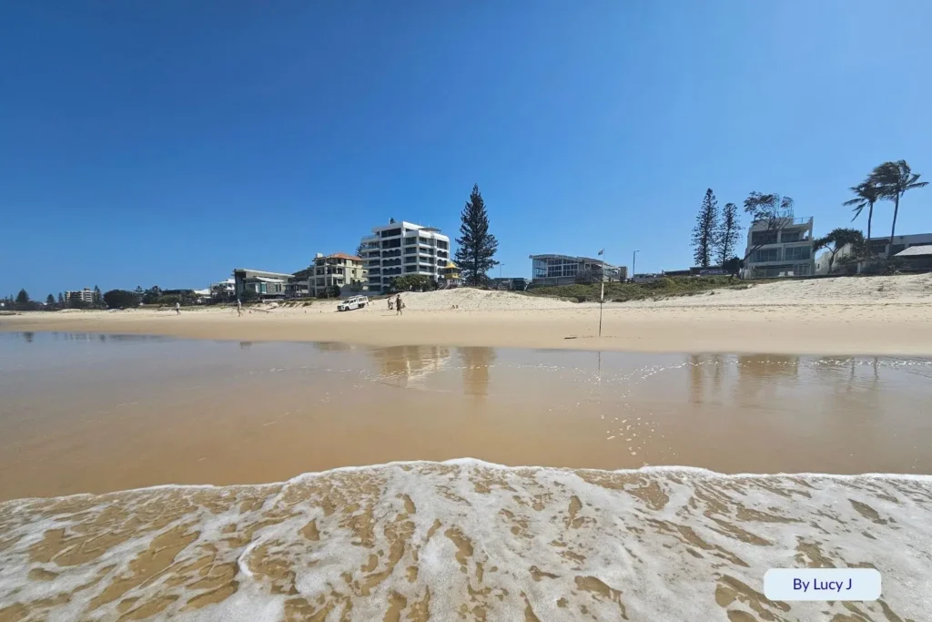 Gentle waves washing ashore in front of beachfront houses at Nobby Beach, Gold Coast, Queensland, under bright blue skies.