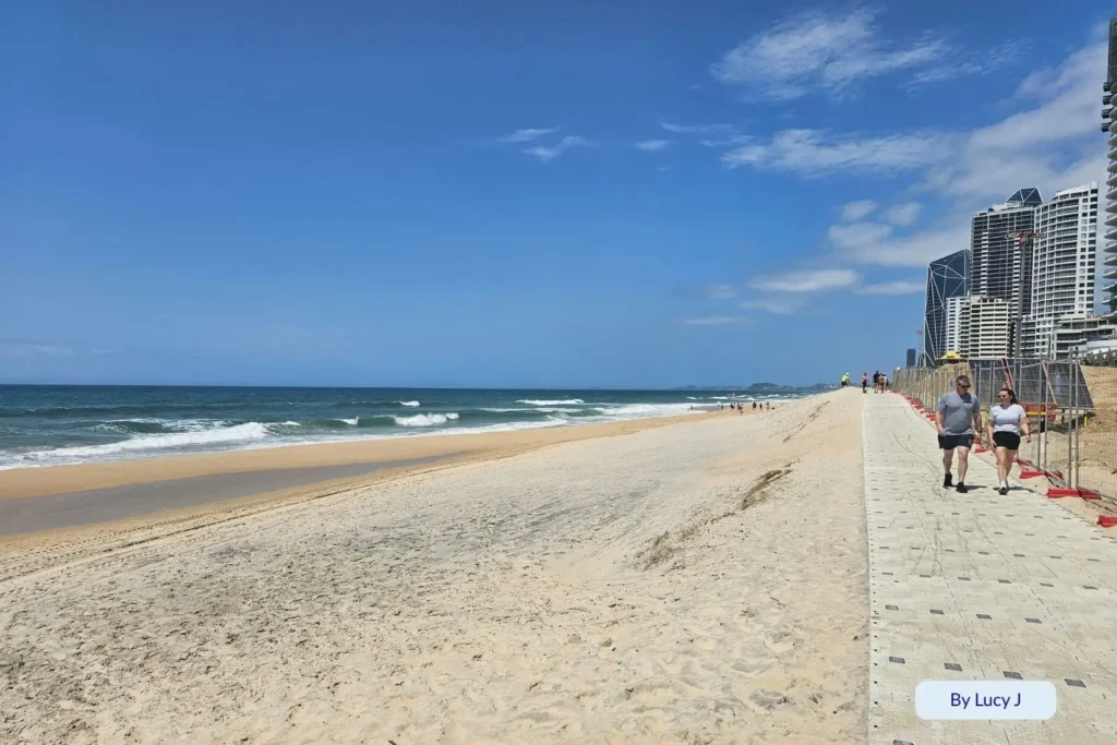 People walking along the sandy path beside Northcliffe Beach with ocean waves and city views, Gold Coast, Queensland, Australia.”