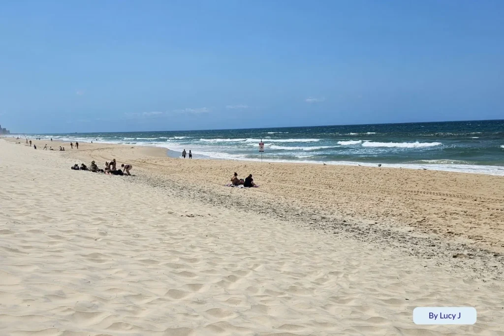 Beachgoers relaxing on the wide sandy shore of Northcliffe Beach under sunny skies with gentle waves along the Gold Coast, Queensland