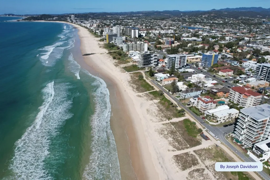 Aerial view of Palm Beach, Gold Coast, Queensland, showing long sandy coastline, ocean waves, and beachfront apartments backed by suburban streets.