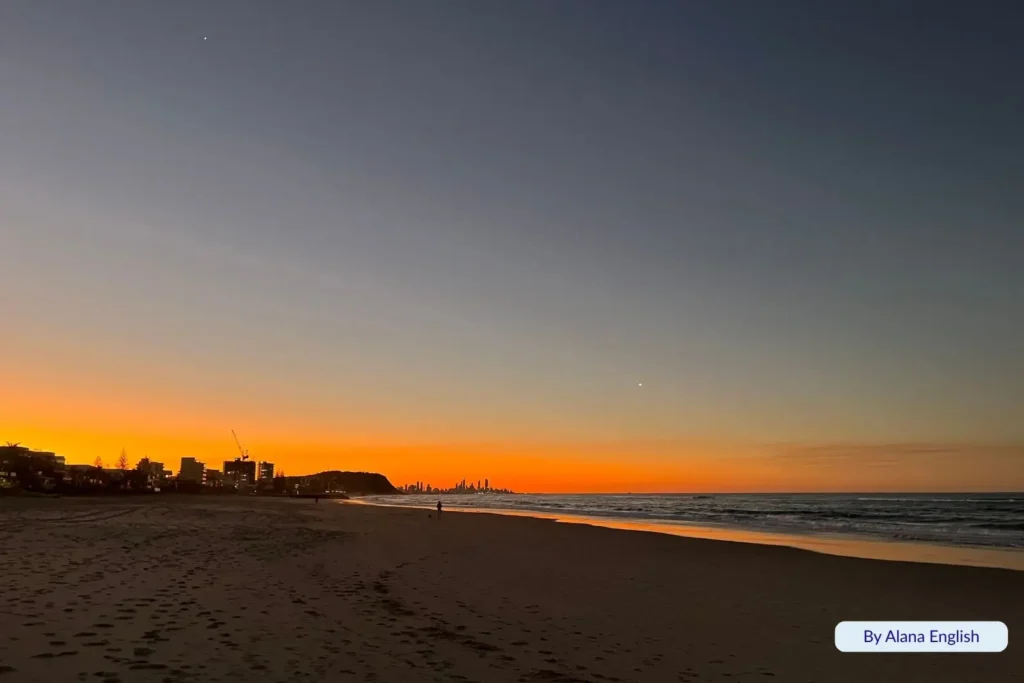 Sunset over Palm Beach, Gold Coast, Queensland, with soft orange skies reflecting on the shoreline and gentle waves rolling onto the sand.