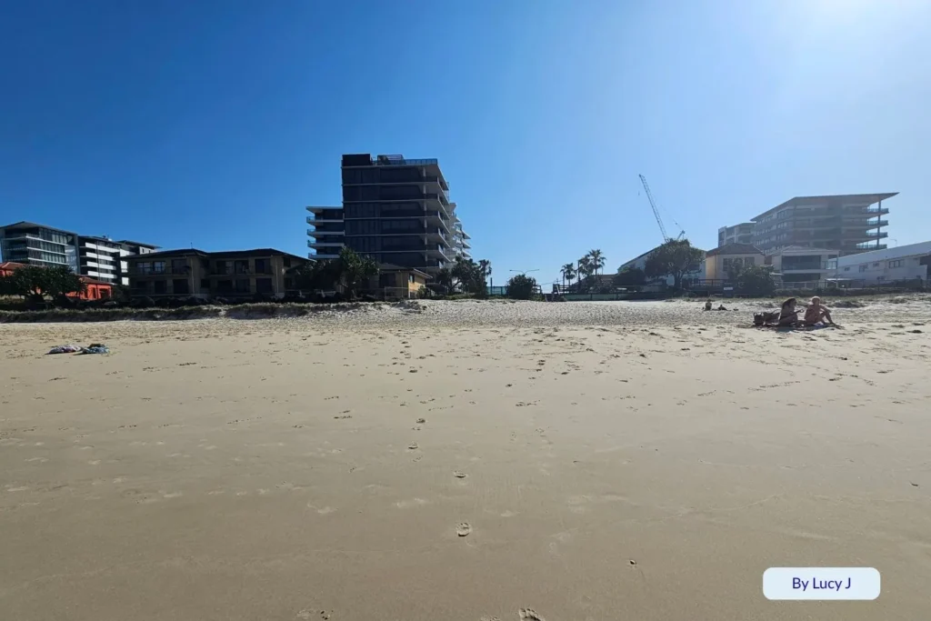 Soft sand and calm shoreline in front of modern beachfront buildings at Palm Beach, Gold Coast, Queensland, under bright blue skies