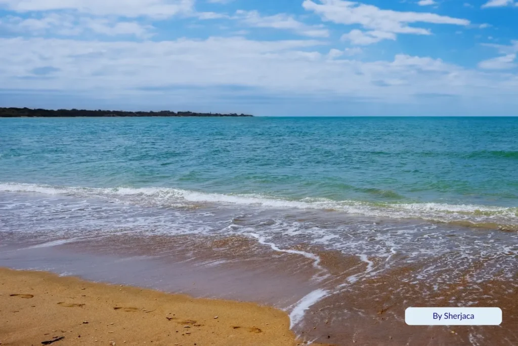 Clear turquoise water and smooth sandy shoreline at Pialba Beach, Hervey Bay, Queensland, under a bright blue sky with light clouds