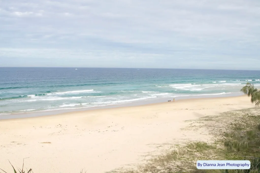 Wide sandy shoreline at Point Cartwright Beach, Sunshine Coast, Queensland — calm waves rolling onto golden sand under soft cloudy skies.