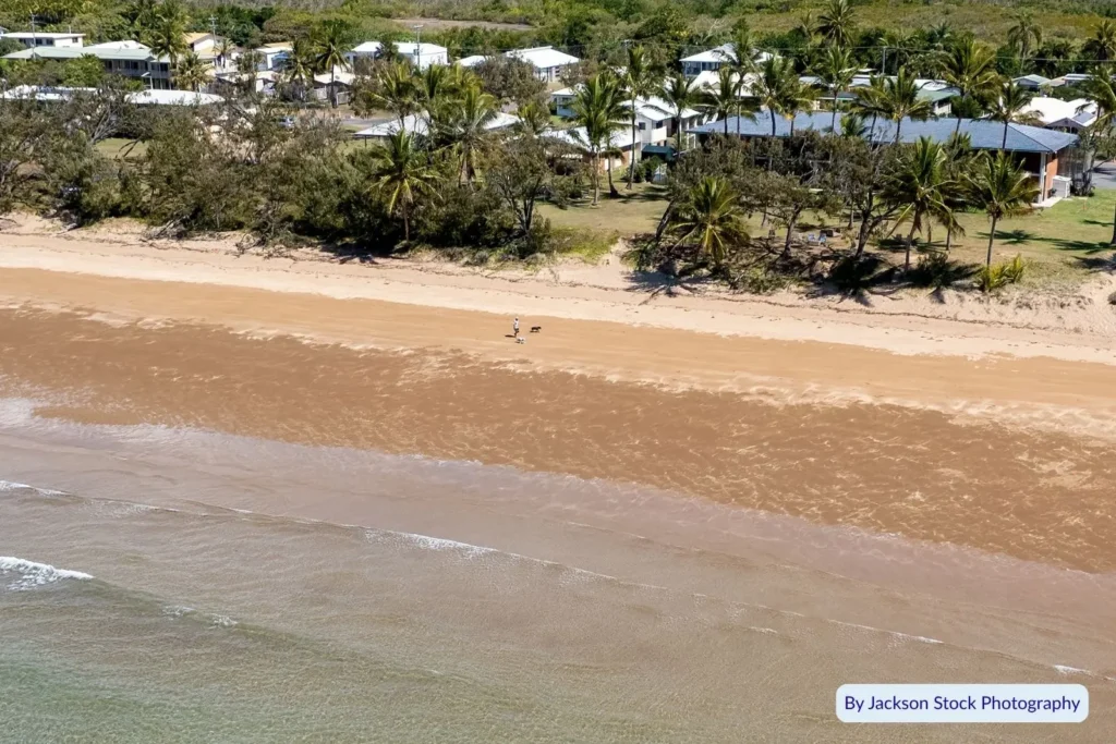 Aerial view of Sarina Beach showing golden sand, gentle waves, and beachfront homes lined with palm trees
