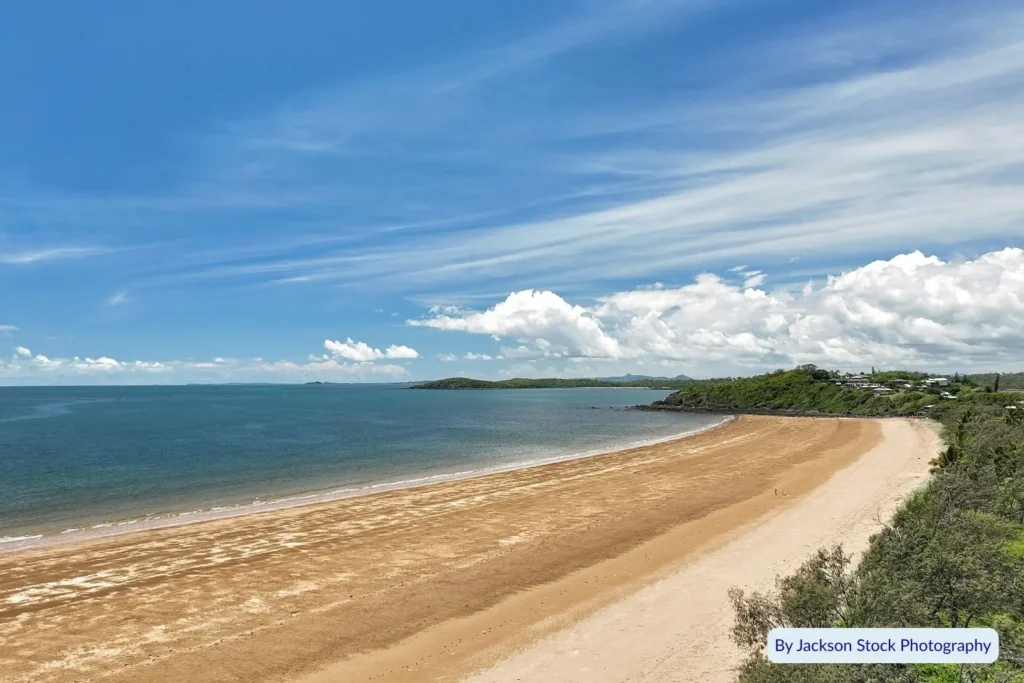 Wide panoramic view of Sarina Beach, Queensland, curving along the coastline with calm blue ocean and clear summer sky.