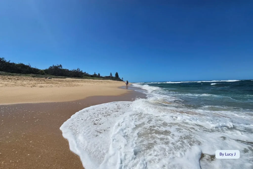 Foamy waves rolling onto the golden sand at Shelly Beach, Caloundra, with clear blue skies and a peaceful Sunshine Coast shoreline in Queensland.