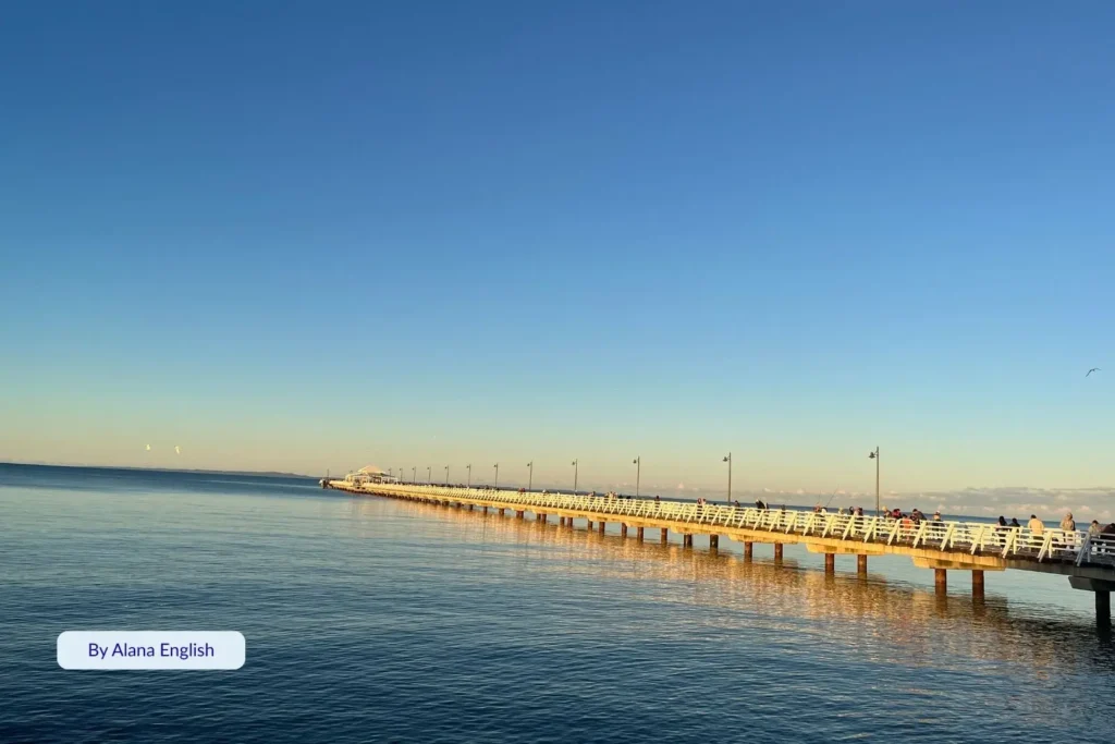 Shorncliffe Pier stretching over calm blue water at sunset with golden sky reflections, Brisbane’s Moreton Bay, Queensland