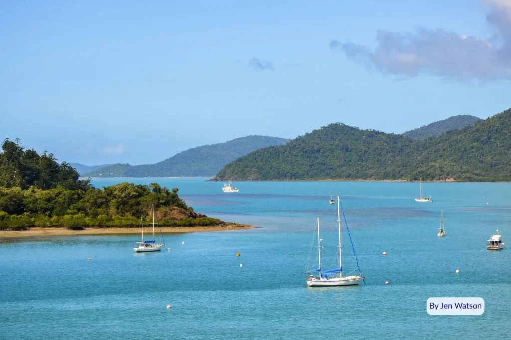 Boats anchored in the calm turquoise waters of Shute Harbour surrounded by lush green hills and islands, Whitsundays, Queensland.