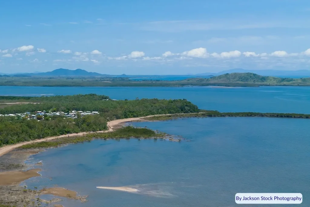 Drone view of St Helens Beach, Queensland, with mangrove-fringed coastline, calm blue water, and distant mountain ranges