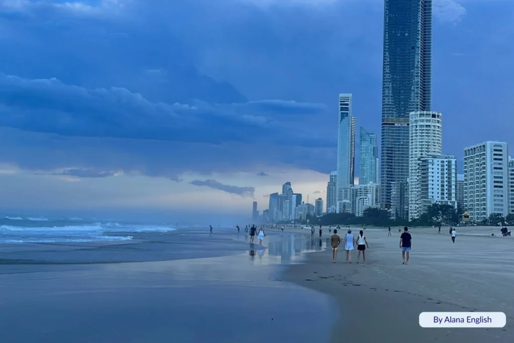 Evening stroll along Surfers Paradise Beach, Gold Coast, with the Q1 Tower and city skyline reflecting under moody blue skies.