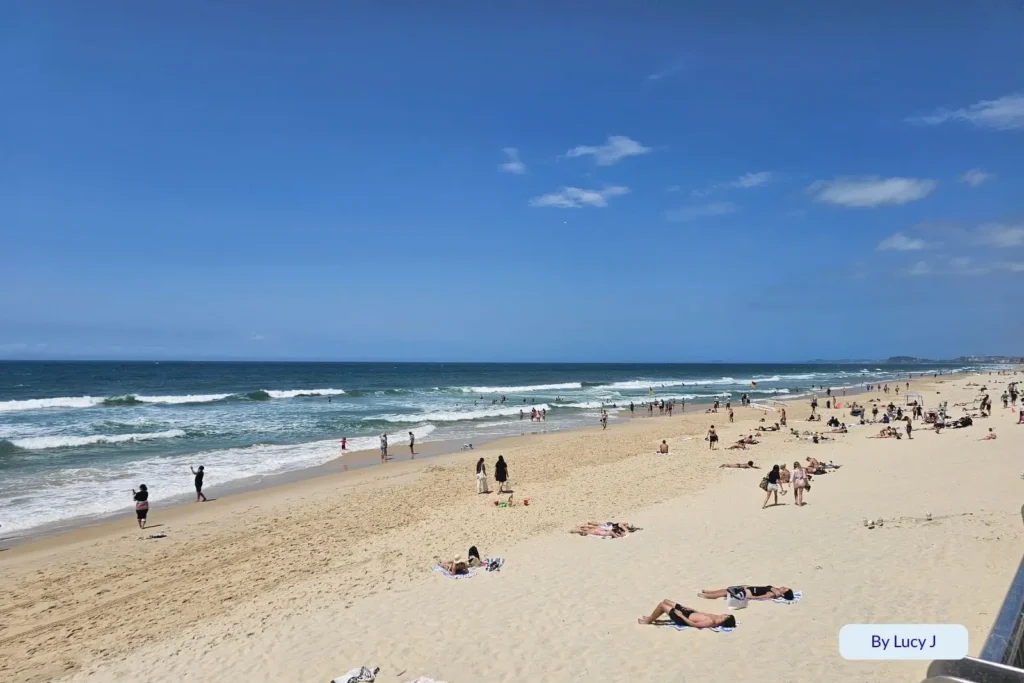 Beachgoers relaxing on the golden sand of Surfers Paradise Beach with gentle surf and blue skies along the Gold Coast, Queensland, Australia