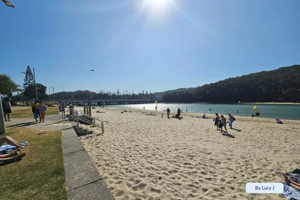 Sunny day at Tallebudgera Creek with people enjoying the beach and grassy picnic area beside the clear blue water, Gold Coast, Queensland.
