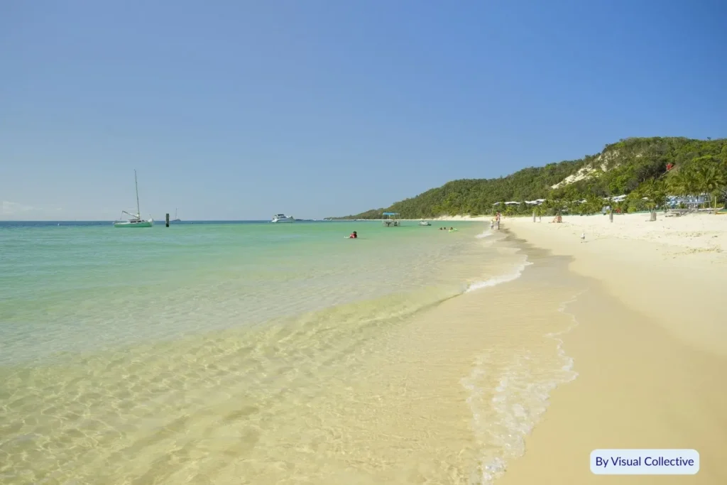 Crystal-clear turquoise water and white sand at Tangalooma Beach on Moreton Island, Queensland, with yachts anchored offshore under a sunny blue sky