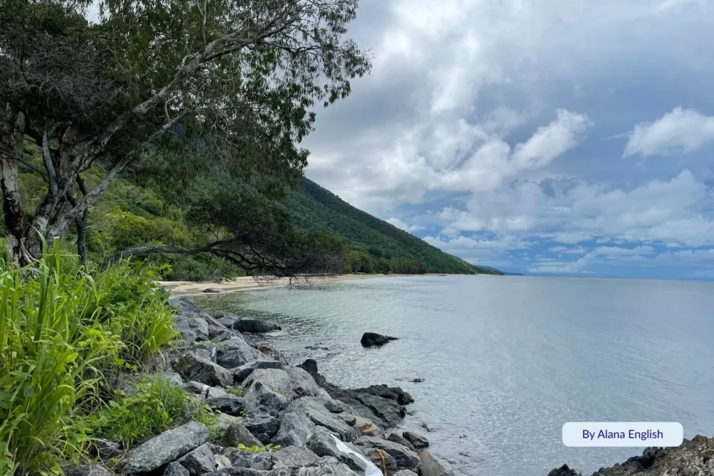 Rocky edge of Trinity Beach with calm turquoise water and cloudy tropical sky, Cairns Queensland.