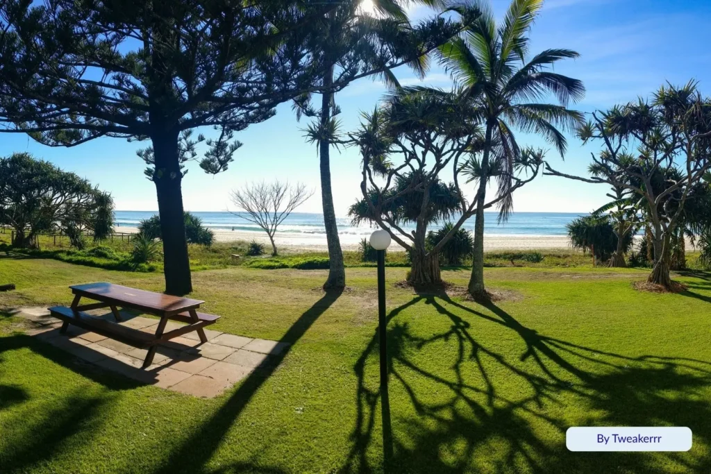 Shaded picnic area surrounded by pandanus and palm trees overlooking the calm ocean at Tugun Beach, Gold Coast, Queensland.