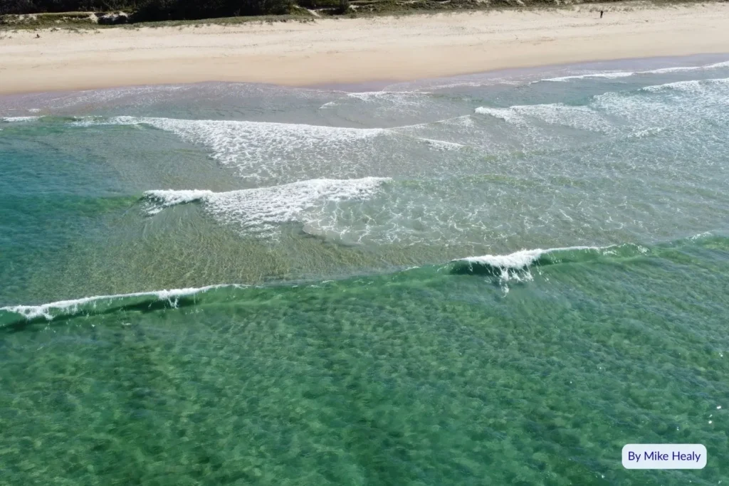 Crystal-clear water and small waves rolling onto the sandy shore at Wurtulla Beach, Sunshine Coast, Queensland
