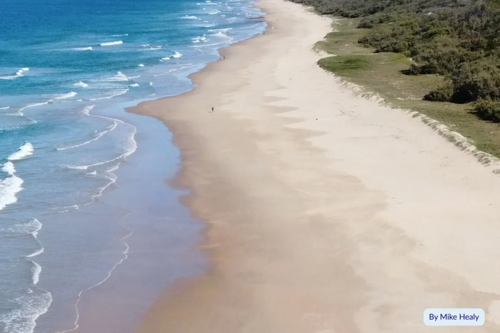 Drone view of Wurtulla Beach, Sunshine Coast, showing golden sand and gentle waves along a quiet coastline