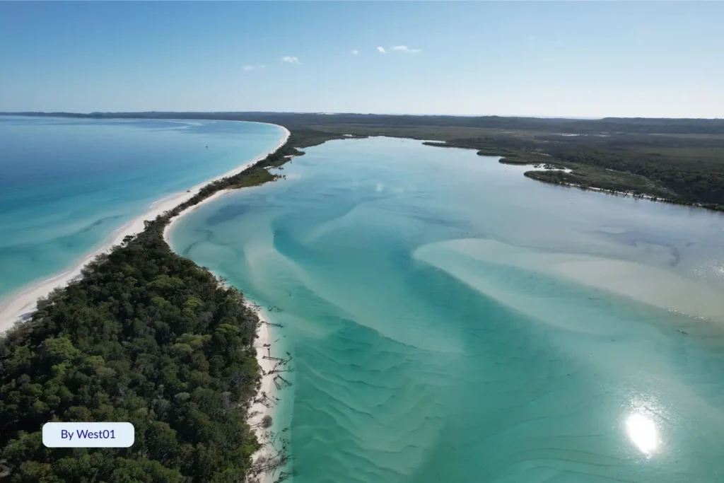Aerial view of Wathumba Creek flowing into Platypus Bay on Fraser Island (K’gari), showing turquoise tidal waters, white sand, and surrounding forest.