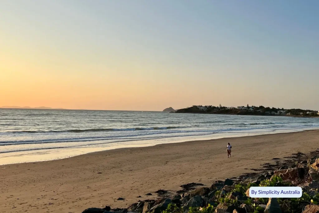 Peaceful sunset at Yeppoon Main Beach with golden light reflecting on the sand and a lone walker by the shoreline