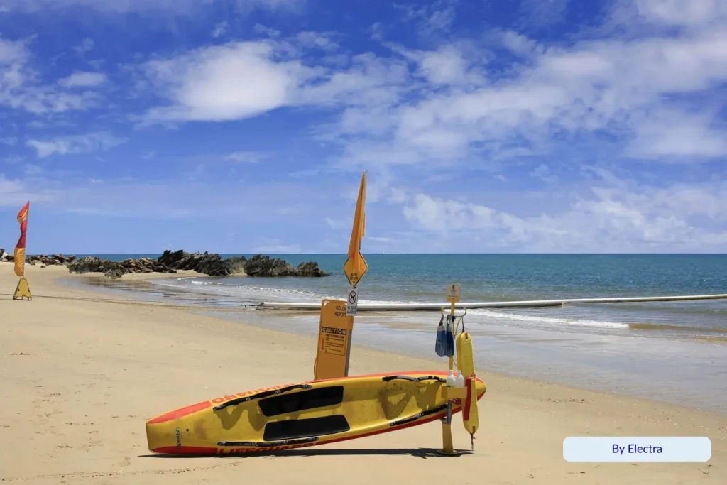 Lifeguard board and safety flags on the golden sands of Yorkeys Knob Beach under a bright blue tropical sky, Cairns Queensland.