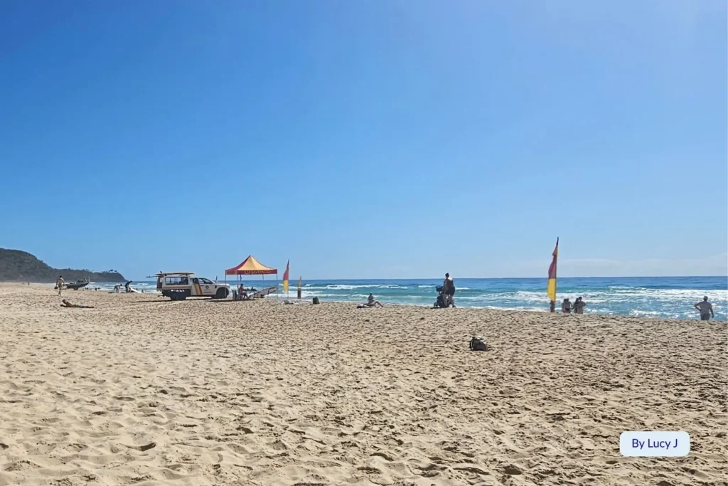 Lifeguard-patrolled Sunshine Beach, Sunshine Coast, Queensland, with golden sand, surf waves, and beachgoers relaxing under a clear blue sky.