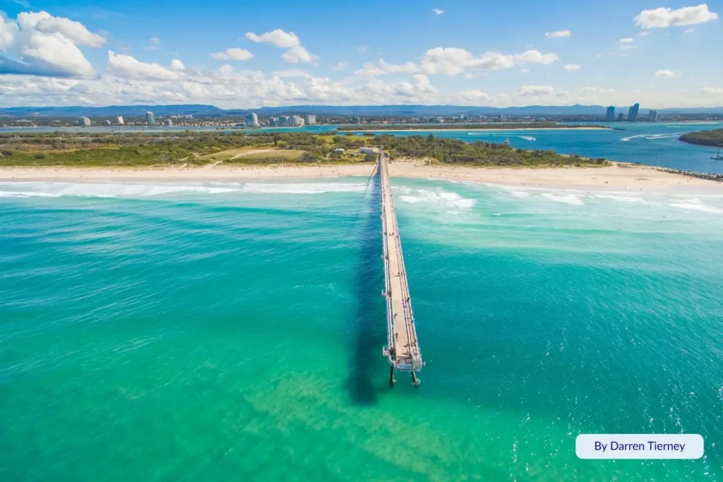 Aerial view of The Spit, Gold Coast, Queensland, featuring the long jetty extending into turquoise waters with golden sand and city skyline in the distance.