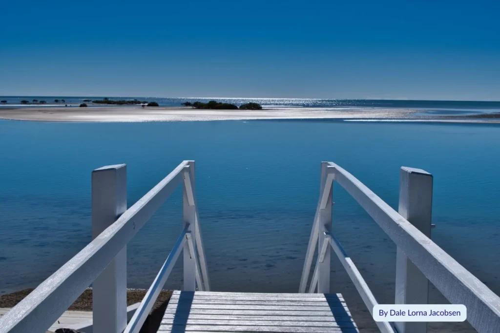 Wooden jetty leading to calm blue water at Toogoom Beach, Hervey Bay, Queensland, on a bright sunny day with sandbanks visible in the distance.