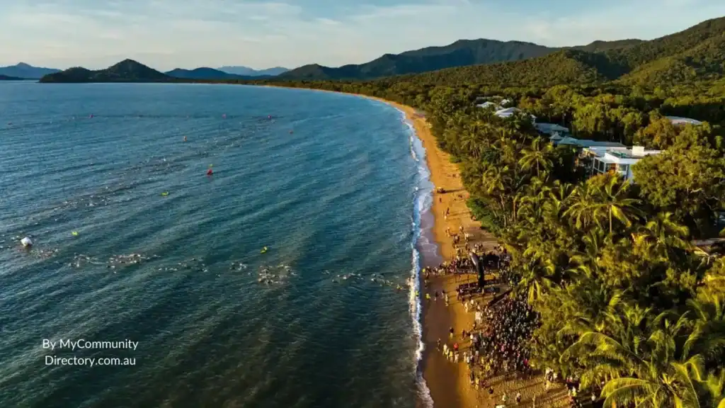 Aerial view of busy tropical beach with swimmers, palm trees and mountains near Cairns northern beaches