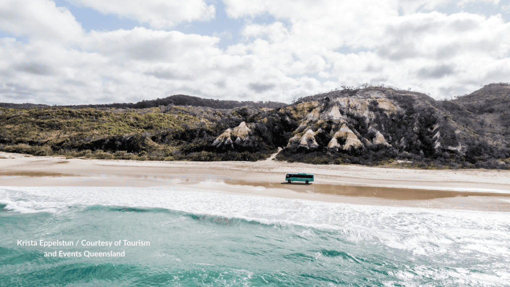 Tour bus on 75 Mile Beach in front of The Pinnacles coloured sand cliffs on Kgari Fraser Island Queensland