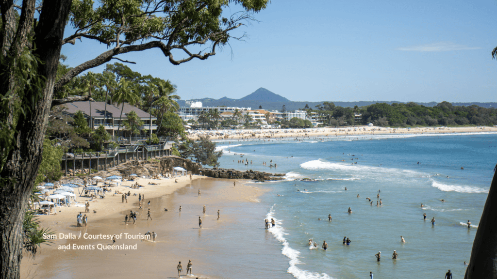 Little Cove Noosa Heads with swimmers on the small sandy cove looking across the rocky point to Noosa Heads Beach and Mount Coolum Queensland