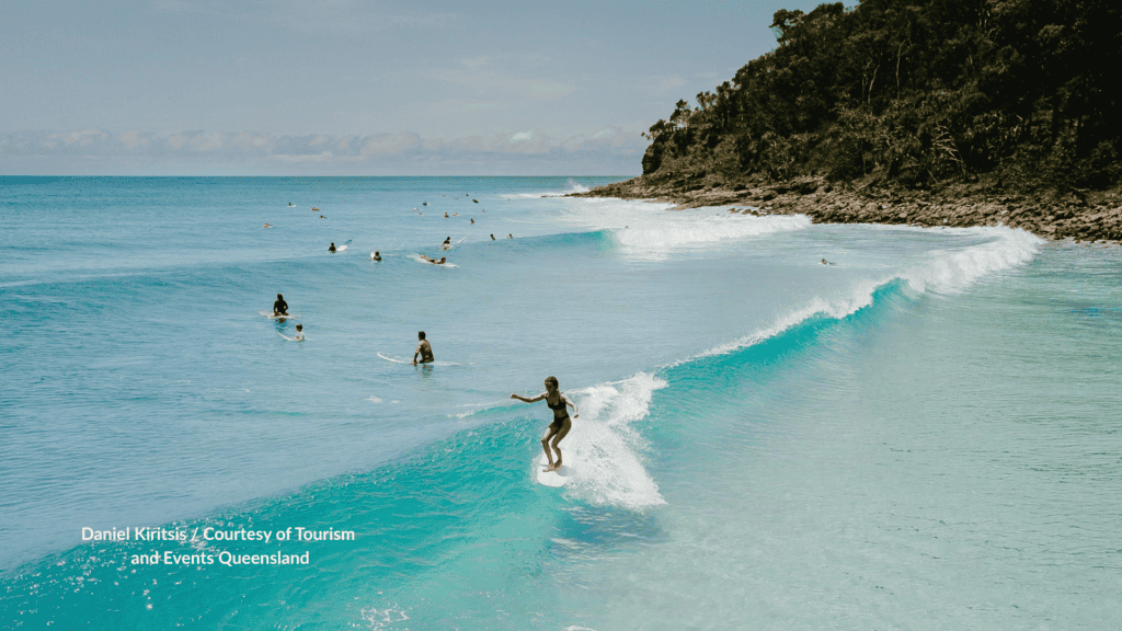 Surfer riding a peeling right hand wave at Noosa Heads Main Beach Queensland toward the rocky national park headland