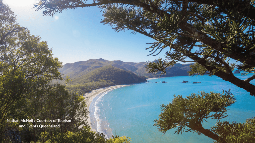 View through the trees at Cape Hillsborough Queensland looking over the curved beach, turquoise bay, rocky islets and forested hills