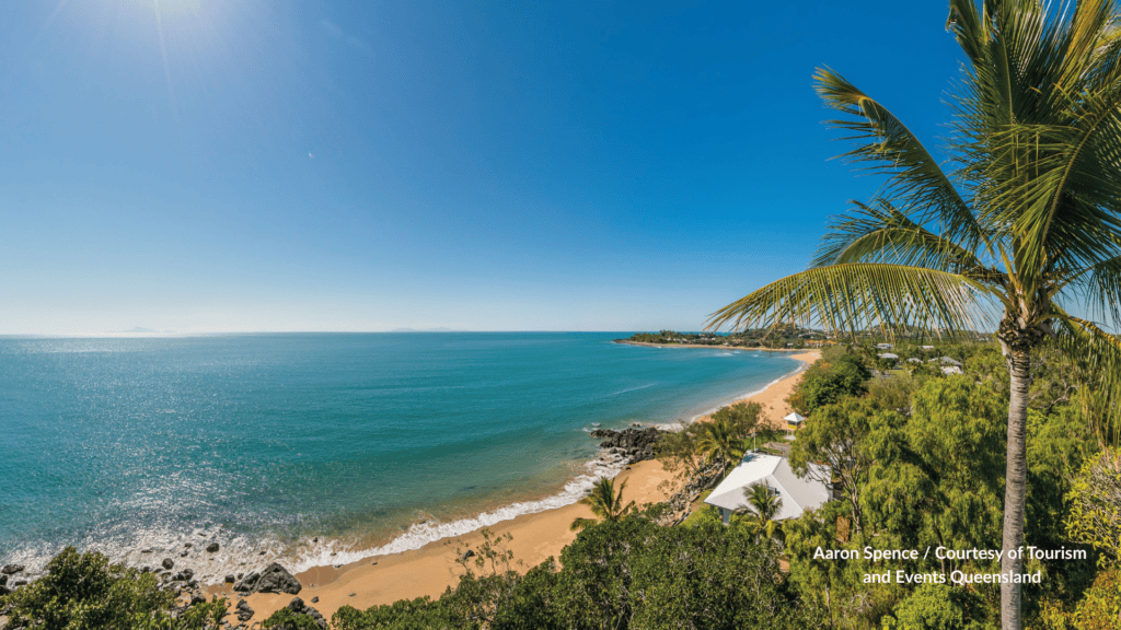 Elevated view of Eimeo Beach Mackay Queensland looking along the sandy bay past palm trees and beachfront houses toward the rocky point and offshore islands