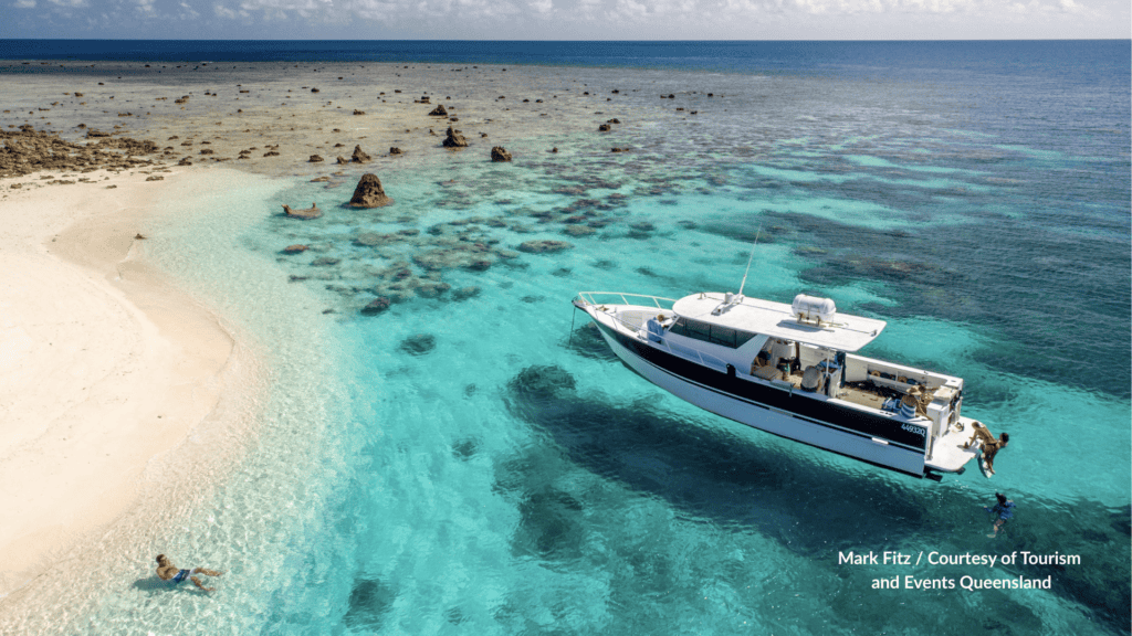 Luxury yacht anchored in turquoise water over coral and white sand at Haggerstone Island Queensland with guests swimming off the stern